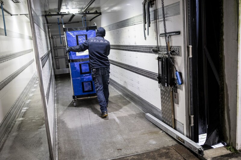 Man in werkkledij duwt kar met goederen in een vrachtwagen
