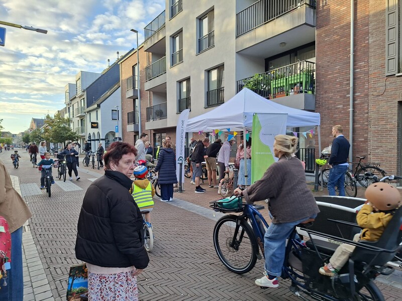 Naar aanleiding van de Strapdag in Stekene staat er aan een drukke straat met verschillende fietsers en voetgangers een partytent en beachvlaggen opgesteld op het voetpad.