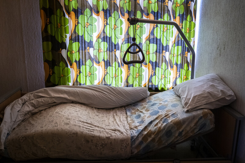 ziekenhuisbed in woonkamer naast 70s-gordijn