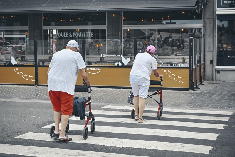 twee ouderen steken in zomerkledij de straat over met een rollator