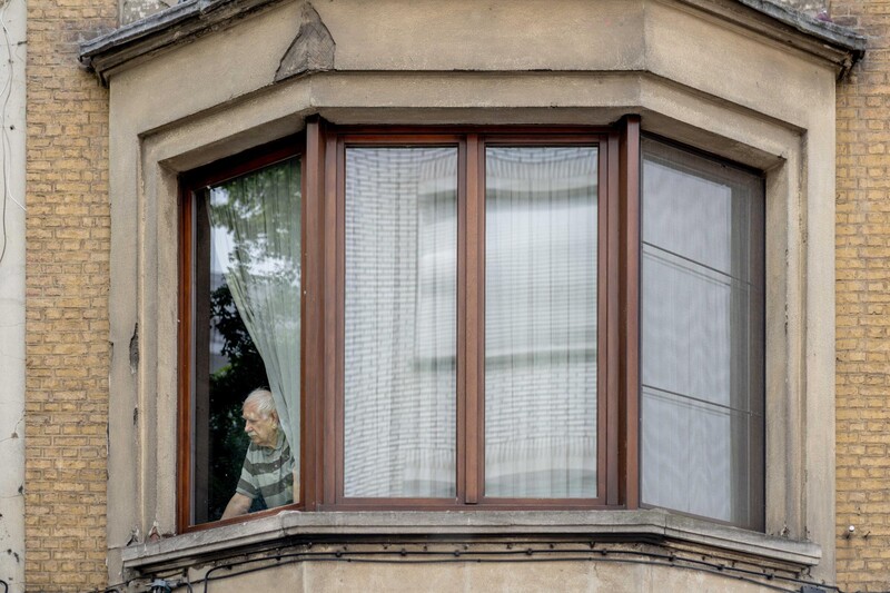 Een oudere man kijkt naar buiten vanuit raam appartement tijdens hittedagen
