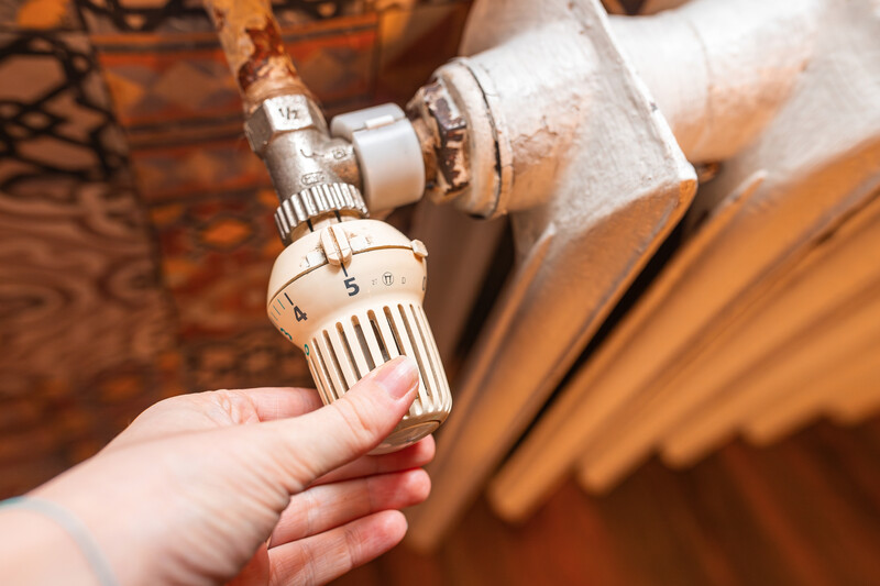 oudere radiator met thermostatische kraan en hand die eraan draait