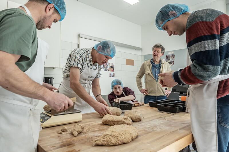 Bewoners van Mariënstede samen aan het werk in de bakkerij terwijl iemand deeg afmeet